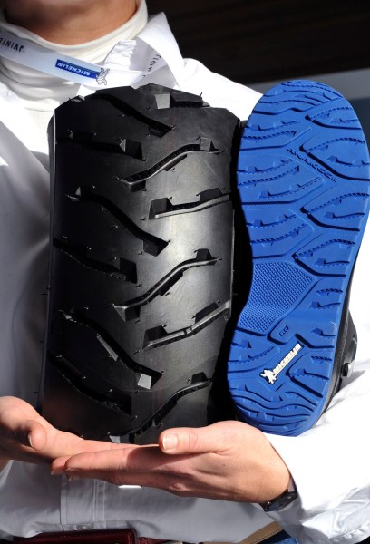 Una persona sostiene un pedazo de un neumático de la motocicleta y un zapato con una suela de goma Michelin después de una conferencia de prensa el 26 de noviembre de 2014 a Centro de Tecnología Michelin en Clermont, Francia para oficializar una asociación entre Michelin y chino técnico de la empresa textil y de la confección Jihua para la fabricación de suelas de zapatos de alta gama. La asociación debe producir inicialmente tres tipos de productos botas de moto , zapatos de ciclismo de montaña y botas de seguridad antideslizante . AFP / THIERRY ZOCCOLAN