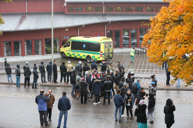 Onlookers stand outside a cordoned area after a masked man attacked people with a sword at a school in Trollhattan