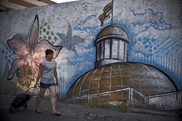 A woman walks past a mural depicting the National Assembly building in Caracas, on December 7, 2015. Venezuela's jubilant opposition vowed Monday to drag the oil-rich country out of its economic crisis and free political prisoners after winning control of congress from socialist President Nicolas Maduro. AFP  PHOTO/Luis Robayo / AFP / LUIS ROBAYO