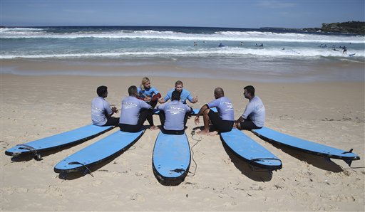 Cinco refugiados (de espaldas) reciben instrucciones de Will Bigelow (centro, de frente) y Conrad Pattinson sobre cómo dominar las olas sobre una tabla de surf en la playa Bondi Beach de Sydney el 23 de marzo del 2016. El surf asoma como una insospechada herramienta terapéutica que ayuda a que refugiados que hicieron traumáticas travesías marinas le pierdan el miedo al mar. (AP Photo/Rob Griffith)