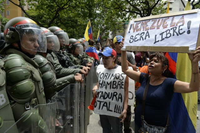 La gente protesta con carteles que decían "Venezuela será libre" y "Nos morimos de hambre. Dictadura total" contra los nuevos poderes de emergencia decretado esta semana por el presidente Nicolás Maduro, frente a una línea de policías en Caracas el 18 de mayo de 2016. Se esperaba ultraje público a derramarse sobre las calles de Venezuela miércoles, con protestas a nivel nacional previstas marca un nuevo punto bajo en regla impopular de Maduro. FEDERICO PARRA / AFP