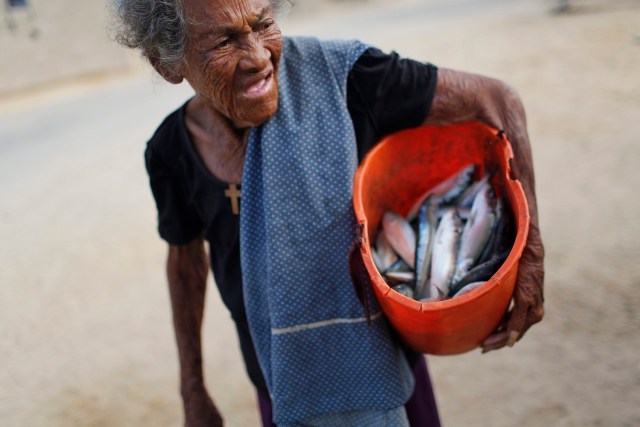 En esta foto del 14 de noviembre de 2016, una mujer lleva una cubeta con pescado que sus vecinos pescadores le dieron de regalo de regreso a su casa, luego de trabajar en Punta de Araya, estado de Sucre, Venezuela. cuando hay momentos difíciles, la capital recibe la mayor parte de los recursos. Eso ha significado que el colapso de la economía se sienta con mayor fuerza en el resto del país, aunque es menos visible. (AP Foto/Rodrigo Abd)