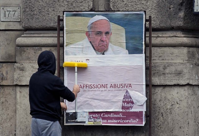 A worker covers with a banner reading "illegal poster" a poster depicting Pope Francis and accusing him of attacking conservative Catholics is seen in Rome, Italy, February 5, 2017. REUTERS/Max Rossi
