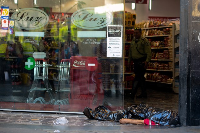 The body of a man lies outside a supermarket, where he died of a heart attack after waiting in a long line to buy food, in Caracas on March 30, 2017. / AFP PHOTO / FEDERICO PARRA