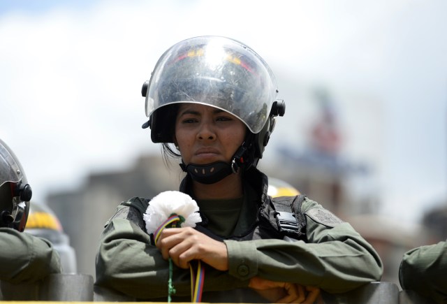 A Venezuelan Bolivarian NAtional Guard member holds a flower during a women's march aimed to keep pressure on President Nicolas Maduro, whose authority is being increasingly challenged by protests and deadly unrest, in Caracas on May 6, 2017. The death toll since April, when the protests intensified after Maduro's administration and the courts stepped up efforts to undermine the opposition, is at least 36 according to prosecutors.  / AFP PHOTO / FEDERICO PARRA