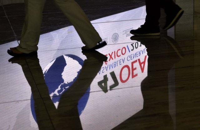 A screen displaying the logo of the 47th General Assembly of the Organization of American States (OAS) is reflected on the floor as people walk by, in the Mexican resort city of Cancun, on June 18, 2017. Foreign ministers from the OAS discuss taking action on the crisis in Venezuela -- a meeting that has infuriated President Nicolas Maduro's government -- ahead of the regional group's general assembly, which runs from Monday through Wednesday. / AFP PHOTO / Pedro PARDO