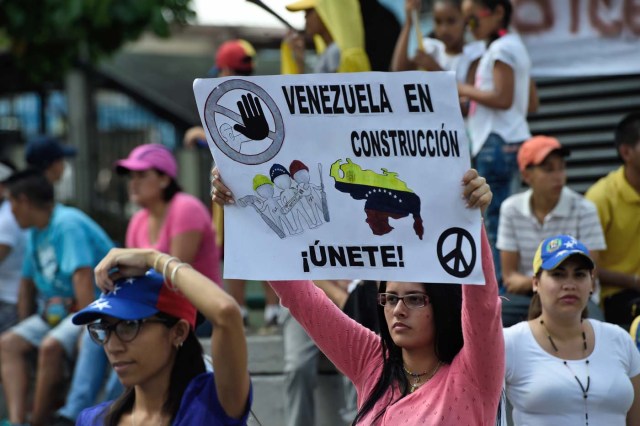 An anti-government demonstrator holds a poster reading "Venezuela Under Construction" in Caracas on July 16, 2017 as she participates in an opposition-organized vote to measure public support for Venezuelan President Nicolas Maduro's plan to rewrite the constitution. Authorities have refused to greenlight the vote that has been presented as an act of civil disobedience and supporters of Maduro are boycotting it. Protests against Maduro since April 1 have brought thousands to the streets demanding elections, but has also left 95 people dead, according to an official toll. / AFP PHOTO / Juan BARRETO