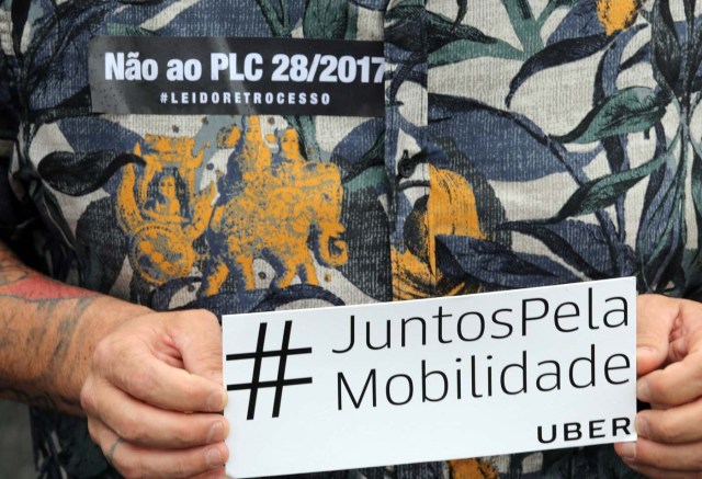 An Uber driver holds a banner during a protest against a legislation threatening the company's business model that is to be voted in Brazil's national congress, in Sao Paulo, Brazil October 30, 2017. The banner reads "#Together for mobility". REUTERS/Paulo Whitaker
