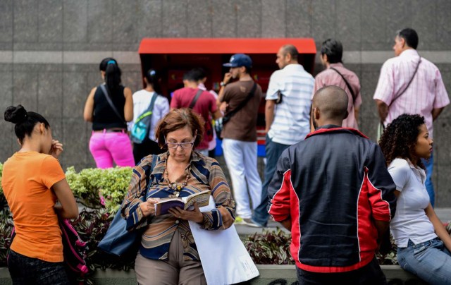 A woman reads as she queues to withdraw money from an ATM in Caracas on November 14, 2017. Venezuela has been declared in "selective default" by Standard and Poor's after failing to make interest payments on bond issues as it tries to refinance its $150 billion foreign debt. / AFP PHOTO / Federico PARRA