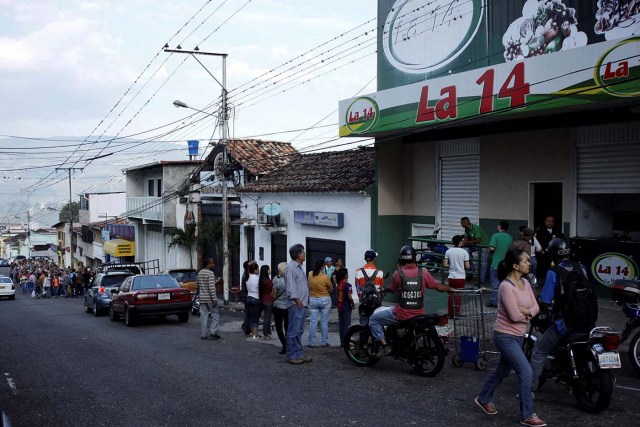 People line up outside a supermarket with its security shutters partially closed as a precaution against riots or lootings, in San Cristobal, Venezuela January 16, 2018. Picture taken January 16, 2018. REUTERS/Carlos Eduardo Ramirez