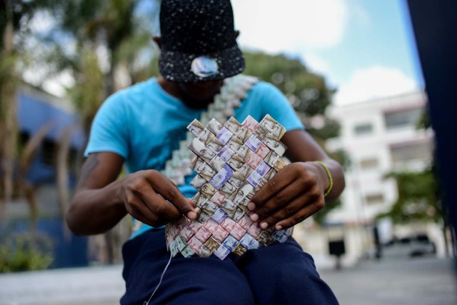 Wilmer Rojas, 25, sists at a bus stop in Caracas as he sews Bolivar bills, to make a paper crown on January 30, 2018. A young Venezuelan tries to make a living out of devalued Bolivar banknotes by making crafts with them. / AFP PHOTO / FEDERICO PARRA