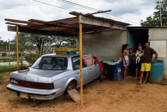 A family stands next to their car out of use due to the lack of spare parts on May 2, 2018 in Maracaibo, Venezuela. Amid blackouts, skyrocketing prices, shortage of food, medicine and transportation, Venezuelans go to elections next May 20 anguished to survive one of the worst crisis in the oil country. / AFP PHOTO / Federico PARRA