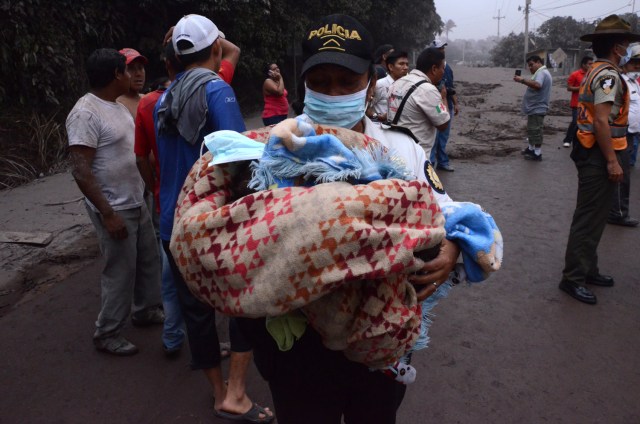 Un oficial de policía carga a un bebé después de la erupción del volcán de Fuego, en el pueblo de El Rodeo, departamento de Escuintla, a 35 km al sur de Ciudad de Guatemala el 3 de junio de 2018. / AFP PHOTO / NOE PEREZ