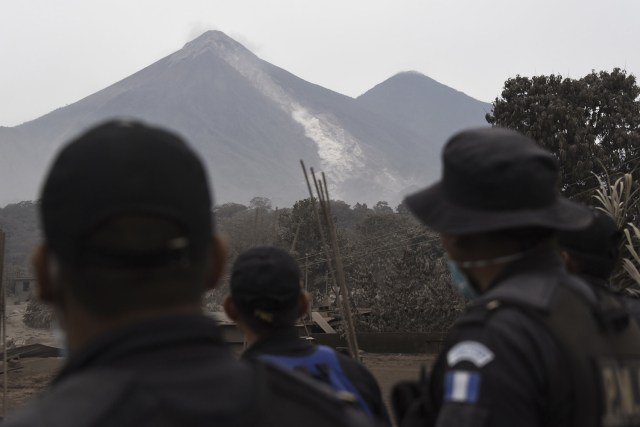 Los oficiales de policía observan el volcán de Fuego desde San Miguel Los Lotes, un pueblo en el departamento de Escuintla, a unos 35 km al suroeste de Ciudad de Guatemala, el 4 de junio de 2018, un día después de una erupción. Al menos 25 personas murieron, según el Coordinador Nacional de Reducción de Desastres (Conred), cuando el volcán Fuego de Guatemala entró en erupción el domingo, eructando cenizas y rocas y obligando al aeropuerto a cerrarse. / AFP PHOTO / Johan ORDONEZ